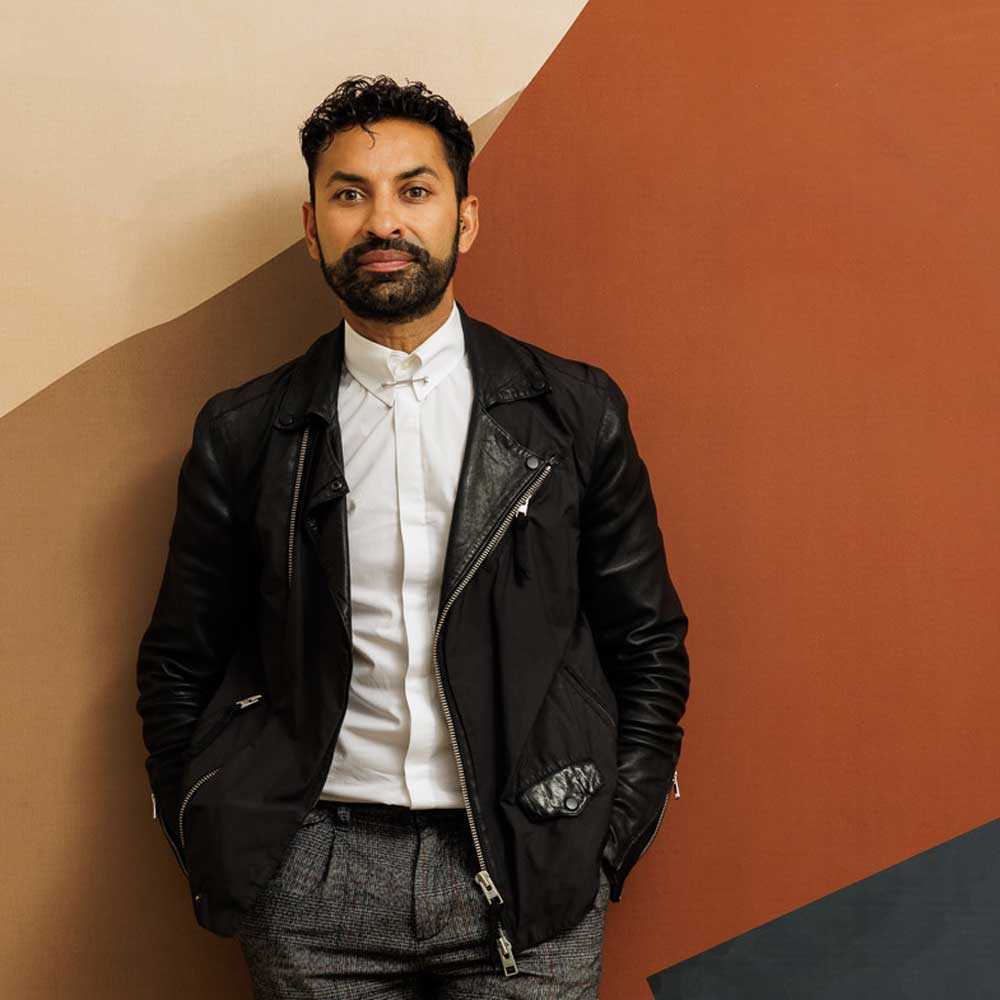 picture of Alykhan Velji a male interior designer with facial hair leaning on a feature wall