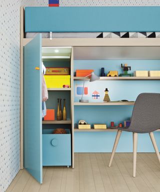 A small walk-in closet adjacent to a desk in a kids room, blue units, shelving and cupboard space
