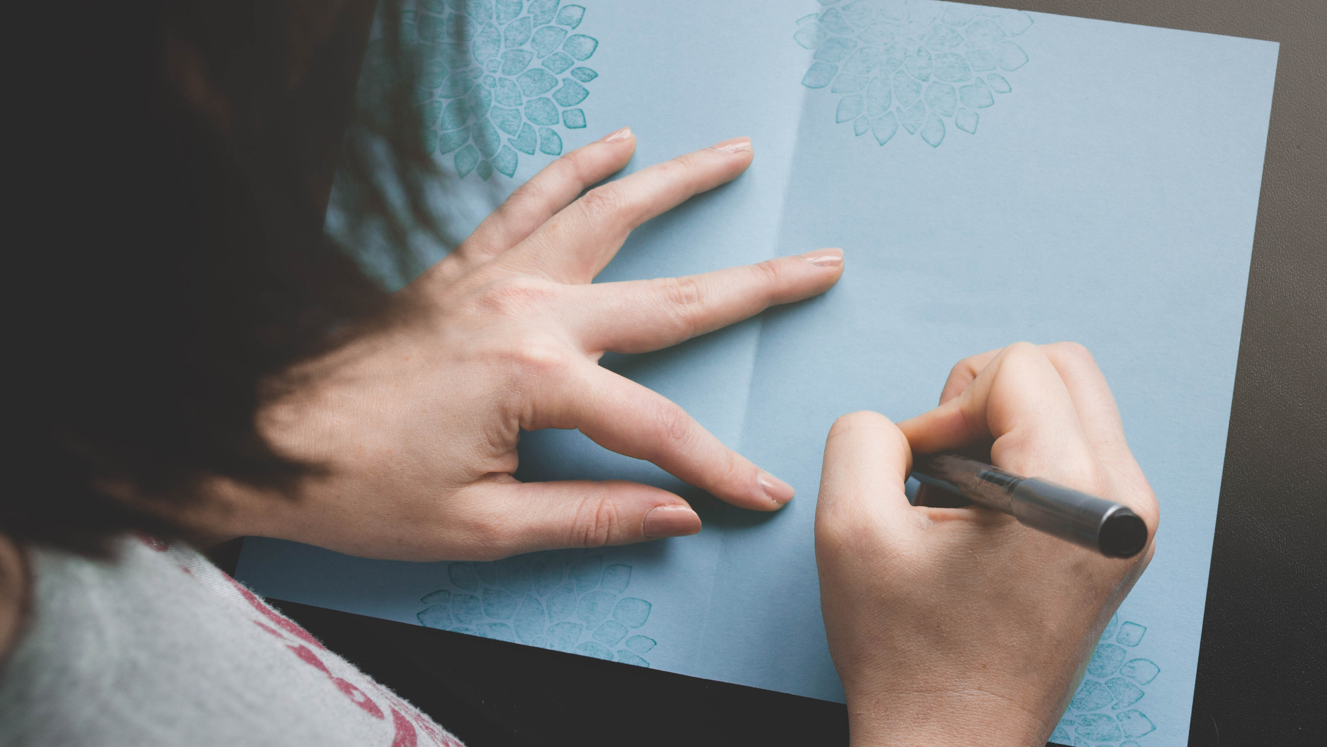 Женщина с темными волосами пишет внутри синей открытки ручной работы