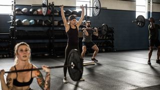 Group of people in gym performing barbell thrusters