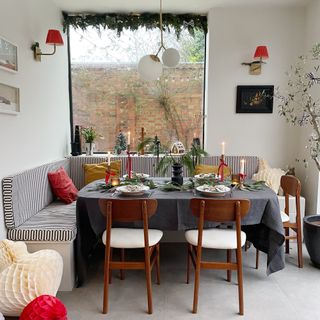 A dining area with a dining table and banquet seating decorated for Christmas with the window behind adorned with a garland hung on a tension rod