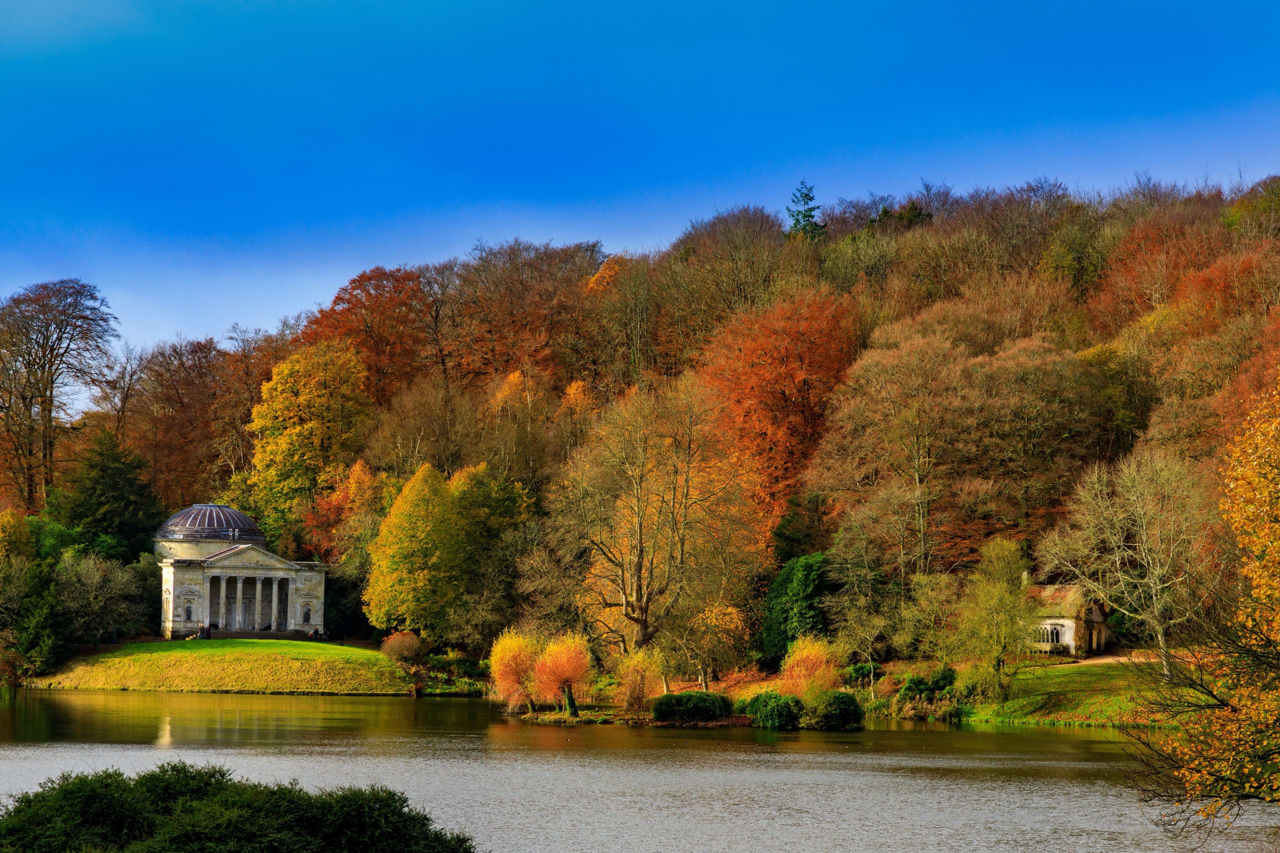 Trees are a rich shade of orange, red and brown, surrounding a lake and pantheon in Stourhead, Wiltshire