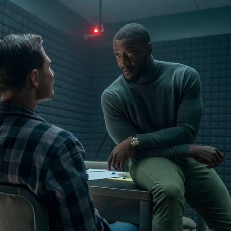 Alex Cross (Aldis Hodge) sits on a desk and faces a suspect sitting in a chair in an interrogation room, in 'Cross.'