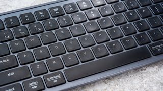 a black and grey budget wireless Bluetooth keyboard with a full-size layout and a numerical keypad is photographed against a blue background