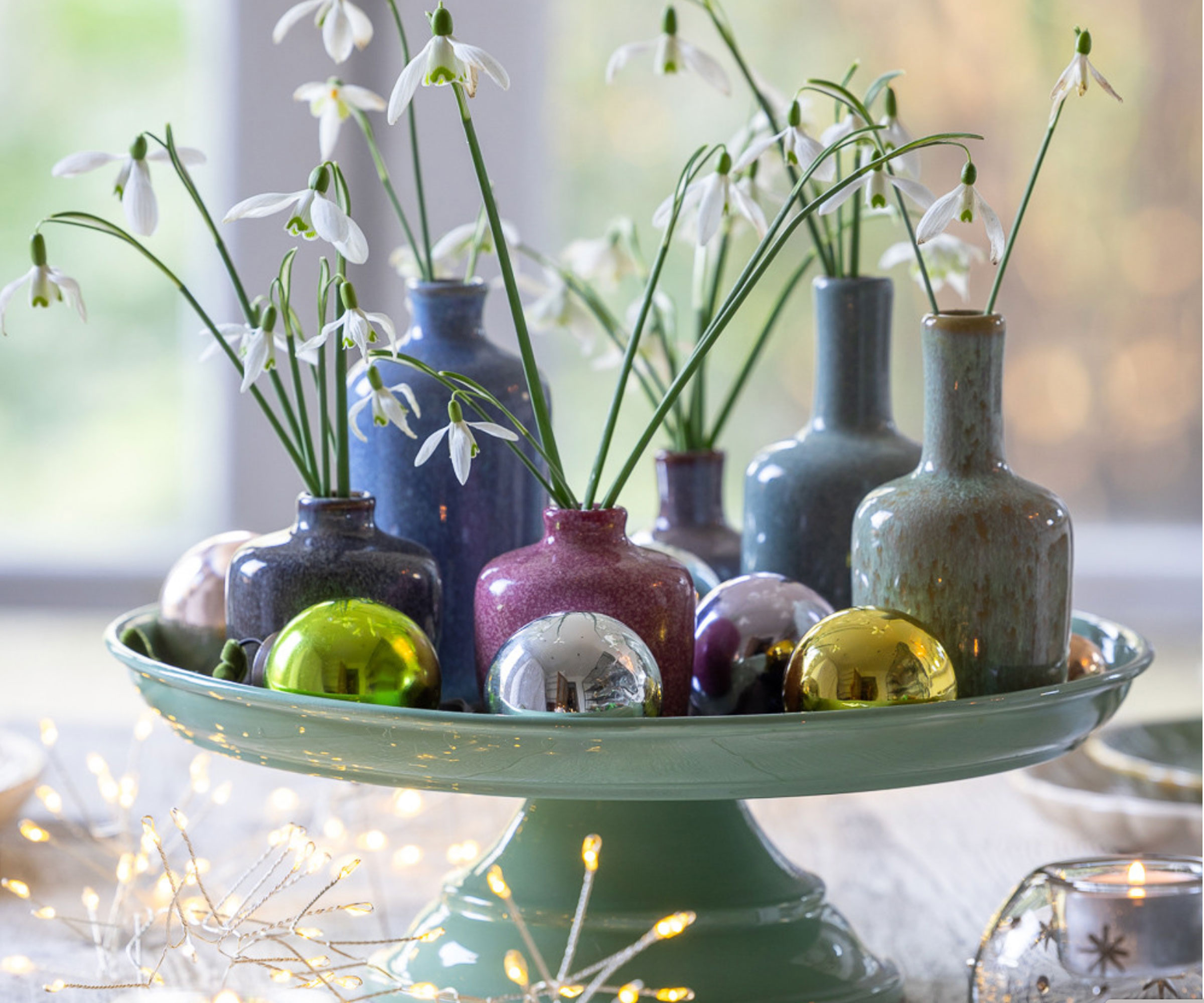 christmas table centrepiece with snowdrops in bud vases, baubles and christmas lights