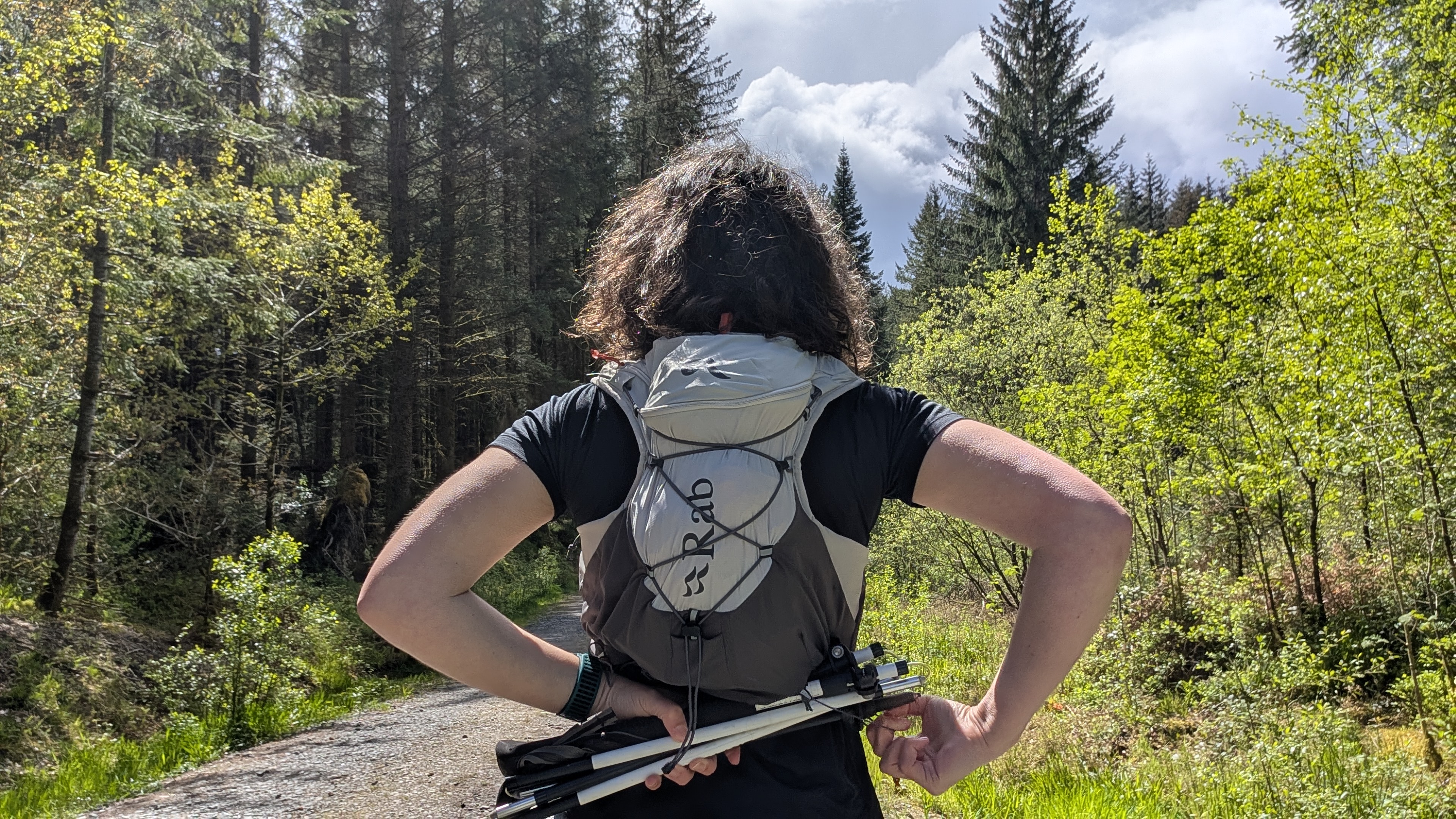 A woman trail runner wearing a black T-shirt, removing her running poles from her grey Rab running vest