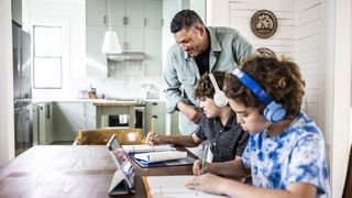 Father helping teen boys with homework at kitchen table