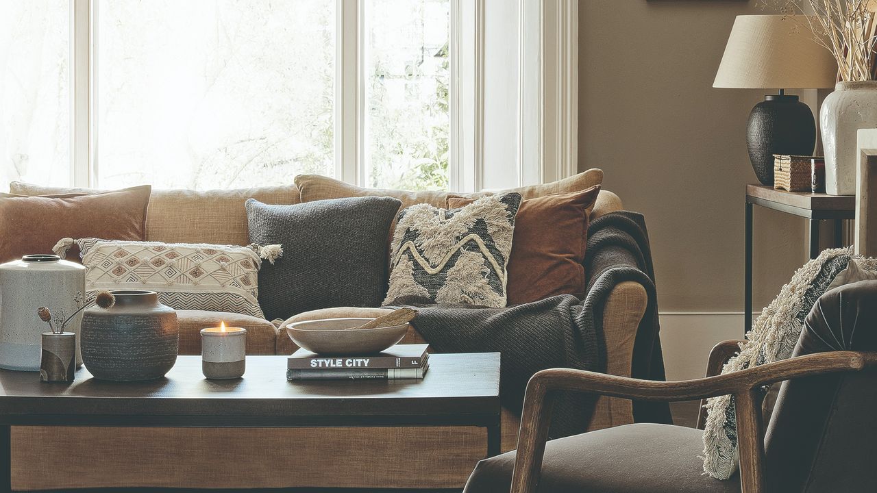 A living room with a light brown sofa with contrasting cushions and a lit scented candle on the coffee table in front of it