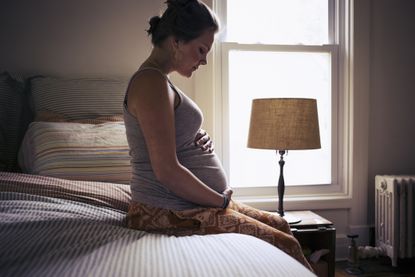 Heavily pregnant woman sitting on a bed at home