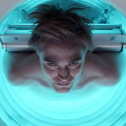 A man (Robert Pattinson) is strapped by his back to a circular machine with a neon glow on the inside, in 'Mickey 17.'