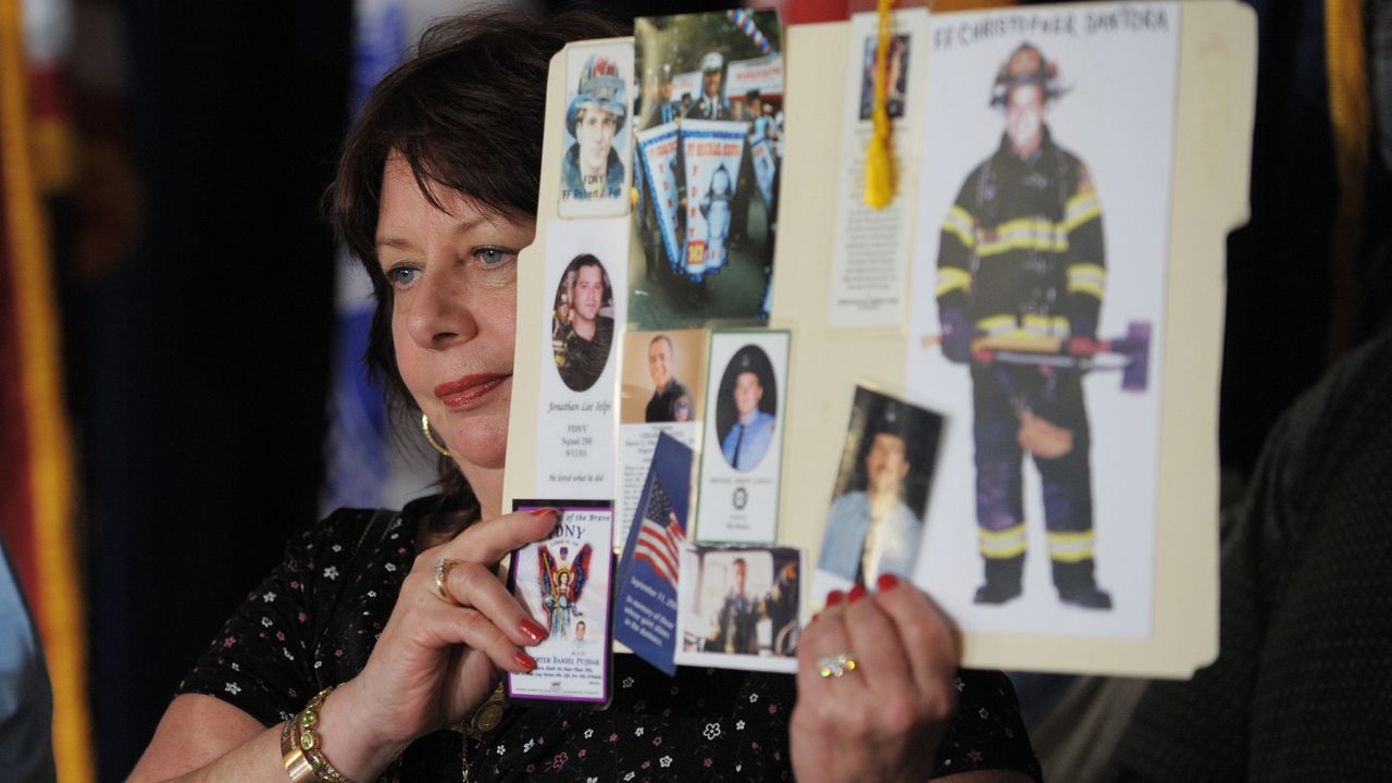 Maureen Santora holds up photos of NYC firefighters killed on 9/11 (including her son) before a pre-trial session for Khalid Sheikh Mohammed in 2008 at Guantanamo Bay. 