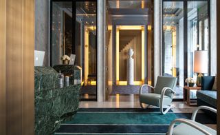 Hotel reception area with green marble desk, striped carpet and blue and green easy chairs