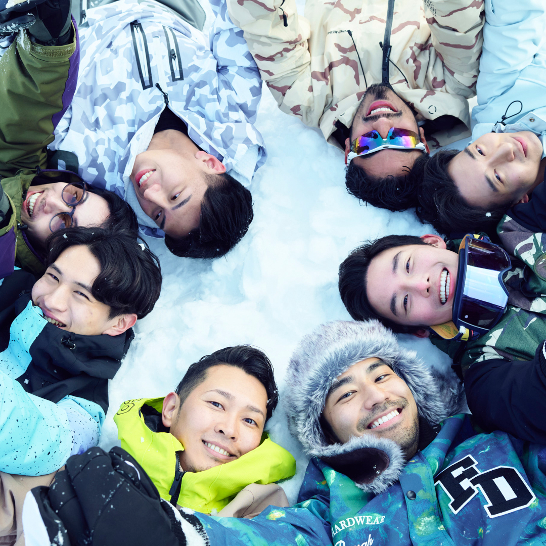 A group of eight Asian men lie in the snow with their heads making a circle, in Netflix's 'The Boyfriend.'