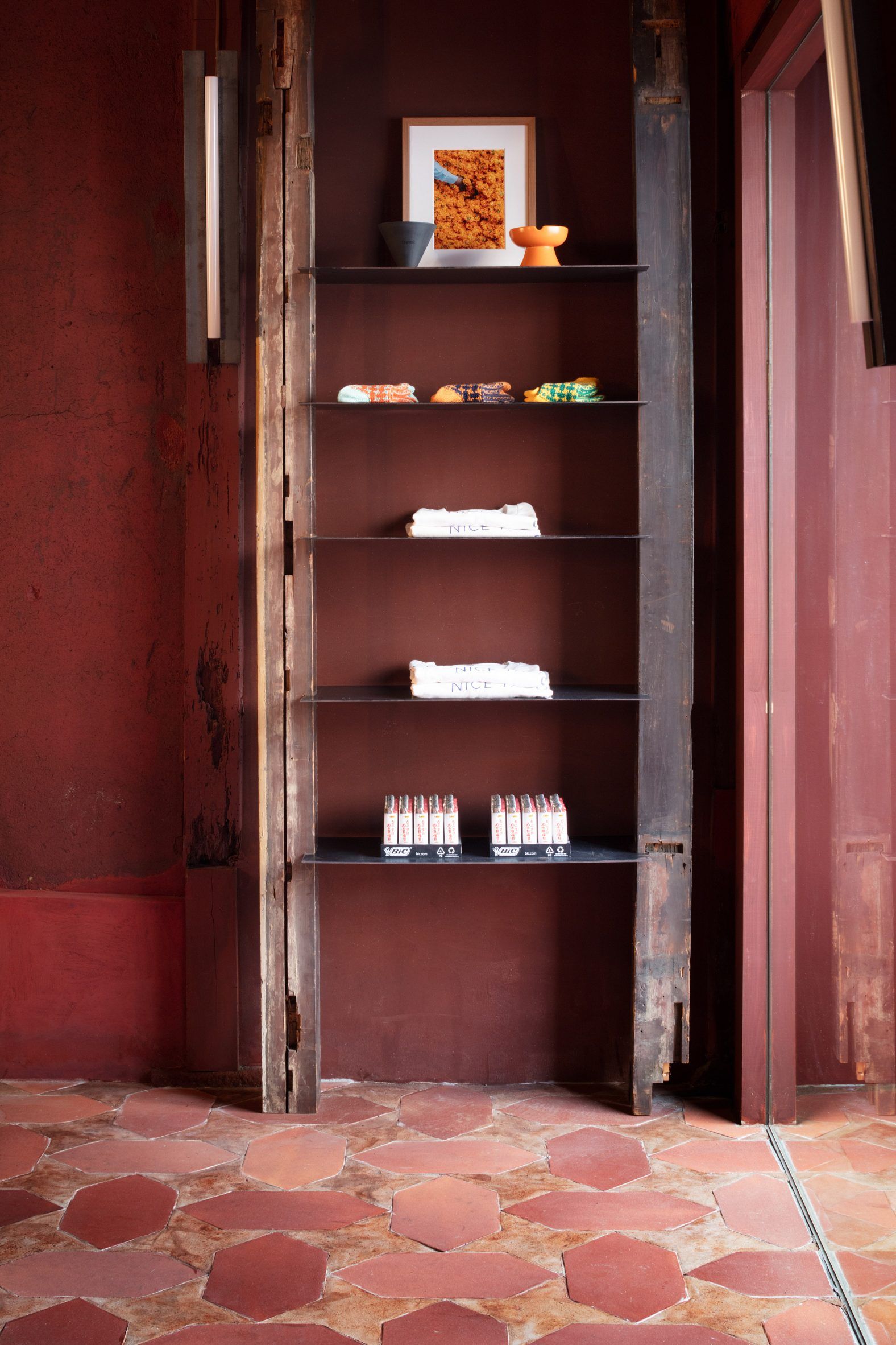 A terracotta-tinted cafe and bar with large, poligonal tiles on the floor, neon lights and sconces, wooden beams and furniture, and a dimly lit ambiance.