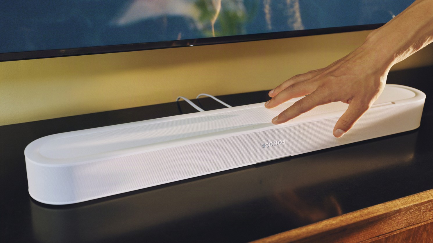 Sonos Beam Ultra on a black table, with someone touching the end with their hand.
