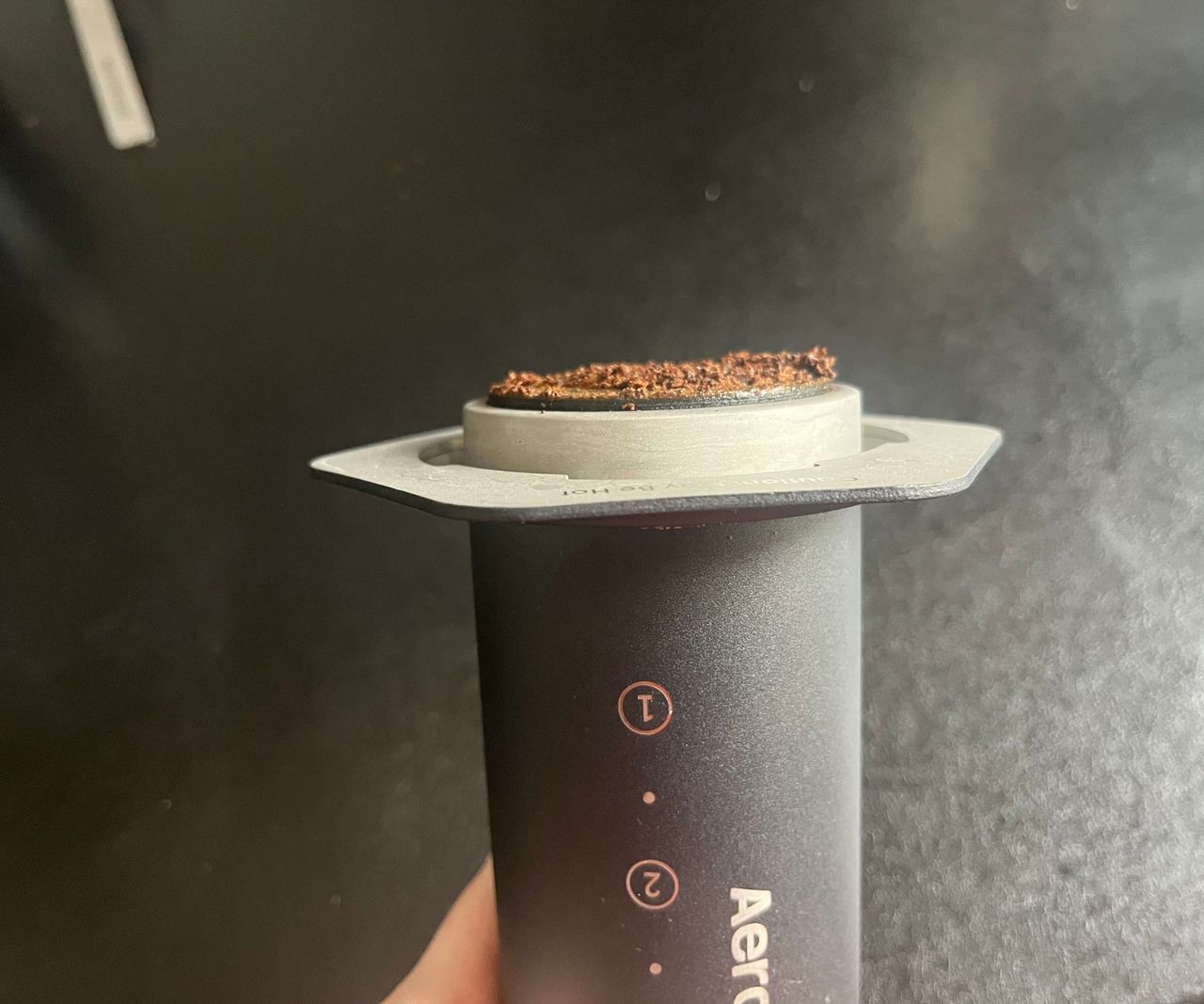 A AeroPress with the plunger pressed all the way through, dried coffee grounds on the end.