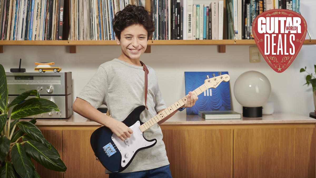 Boy plays small black electric guitar in front of a vinyl record shelf