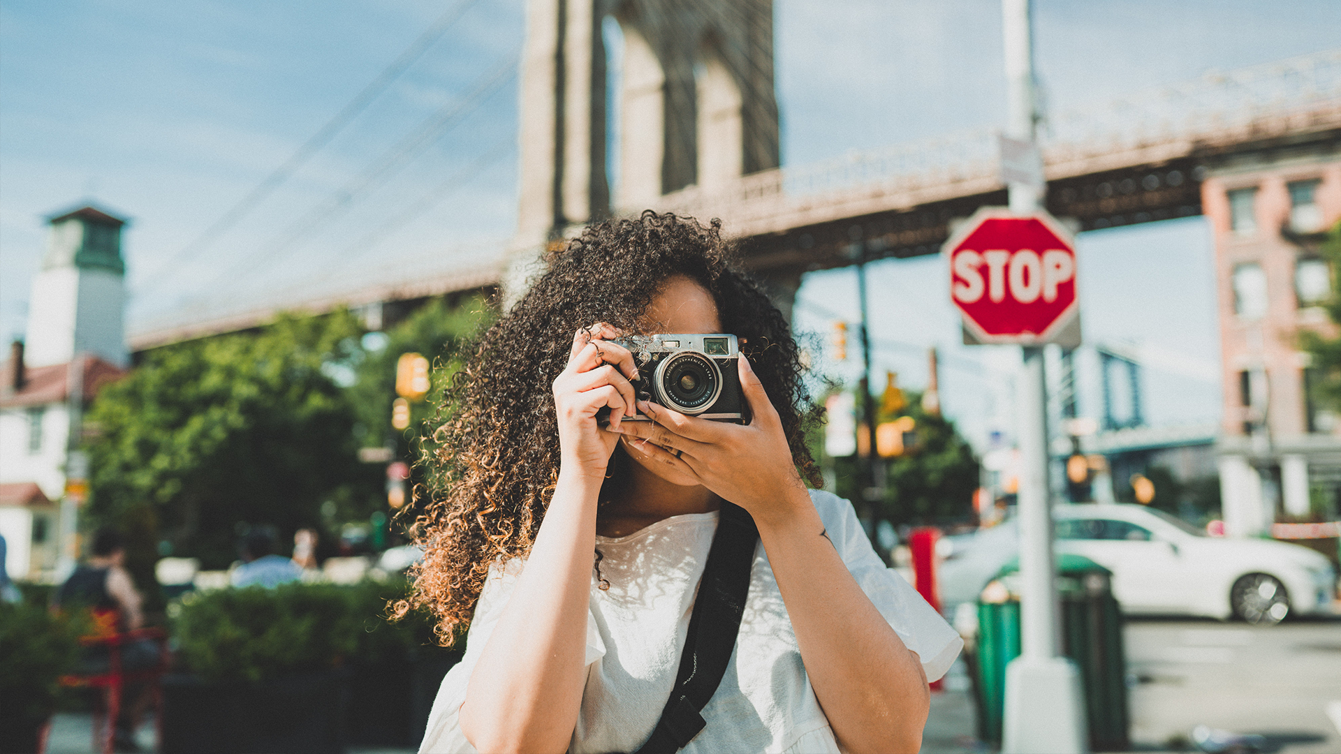 Woman holding camera to take a photo in front of a bridge