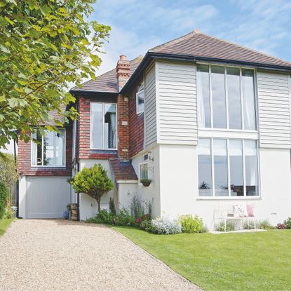 Gravel driveway leading up to house with large windows, and partial cladding and render
