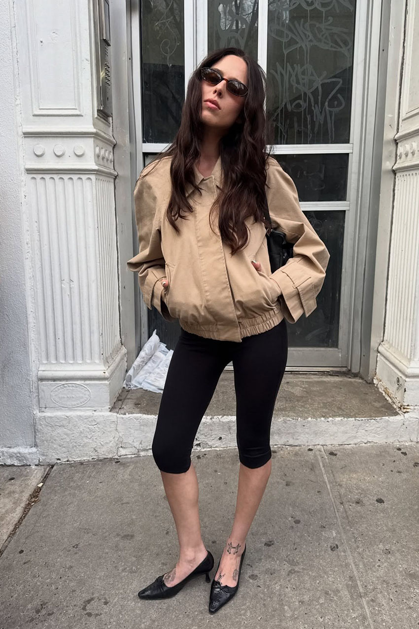 a woman wearing a tan jacket, black capri pants, and black pointed-toe heels