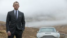 Daniel Craig as James Bond standing next to his Aston Martin in Skyfall