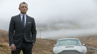 Daniel Craig as James Bond standing next to his Aston Martin in Skyfall
