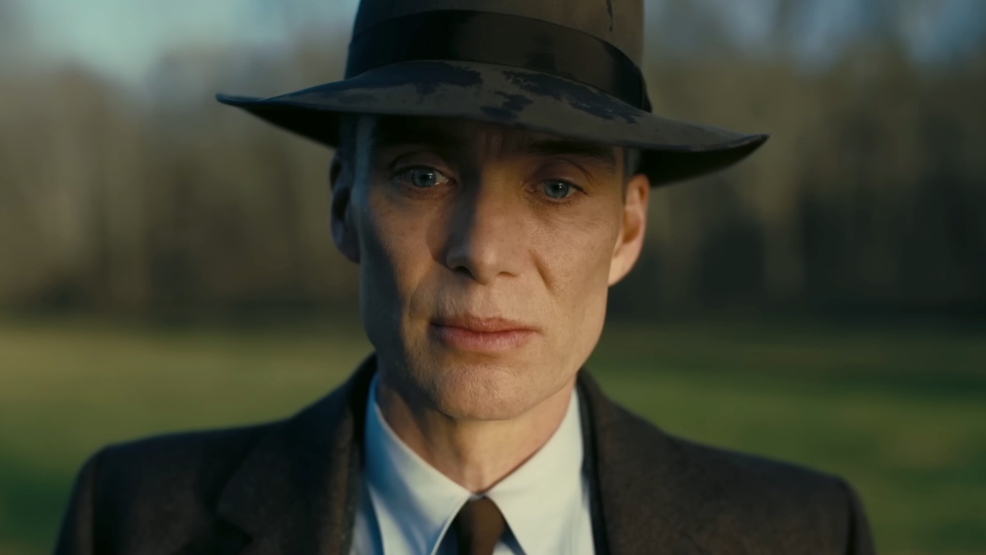 A close up on Cillian Murphy looking sad, wearing a dark suit and dark fedora in Oppenheimer