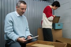 Middle Aged Man Packing Boxes While Young Adult Man Organizing Items 