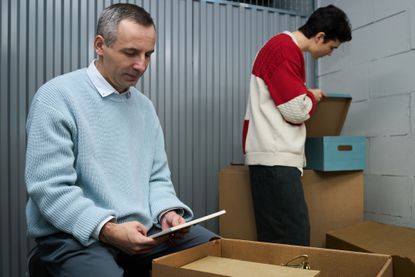 Middle Aged Man Packing Boxes While Young Adult Man Organizing Items 