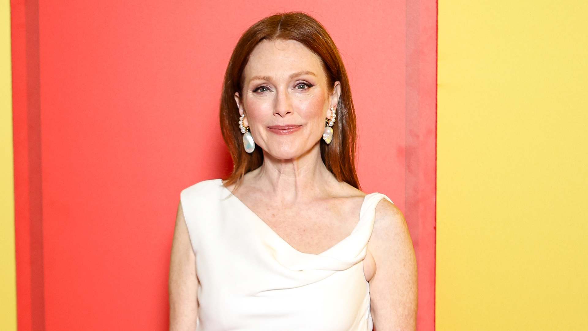 Julianne Moore wearing a white dress and dangly pearl earrings with her red hair styled to fall over her shoulders.