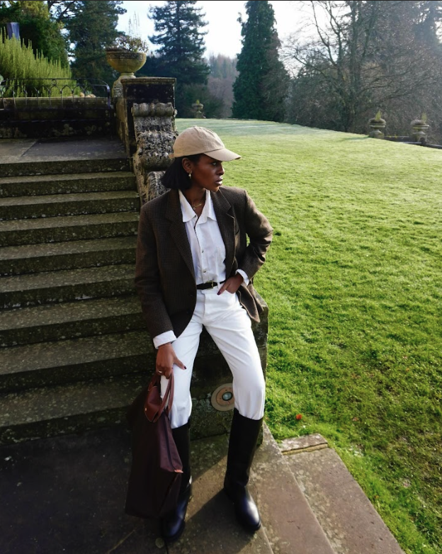 Georgia wears a beige hat, white button-down, brown blazer, white jeans, and black riding boots.