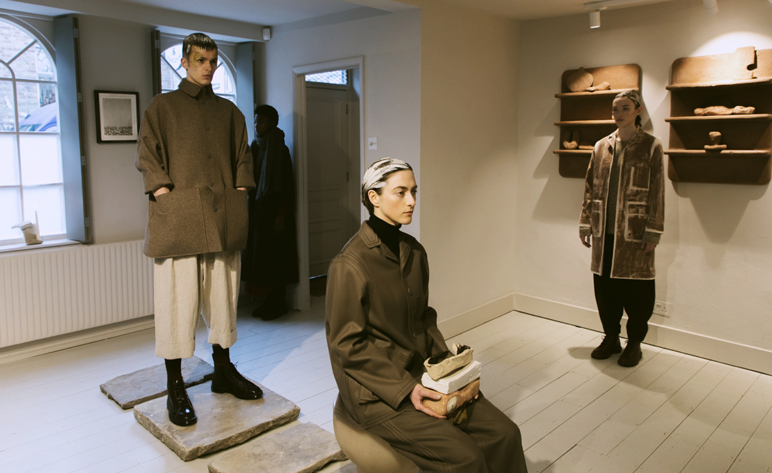 Models stand on plinths, in beige trousers and heavy tailored coats
