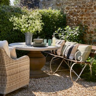 small walled courtyard garden with traditional style wicker chair, wrought iron bench and stone topped round table