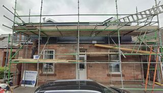 A builder on scaffolding carrying out work on a two-storey house