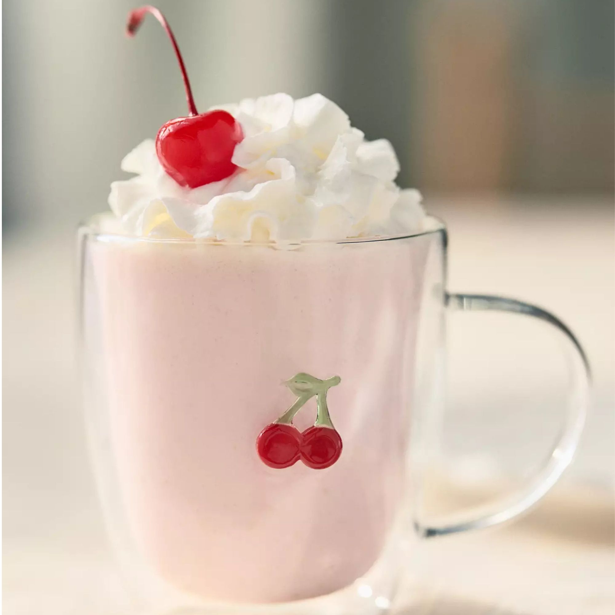 Glass mug with small cherry design, filled with a strawberry milkshake and whipped cream