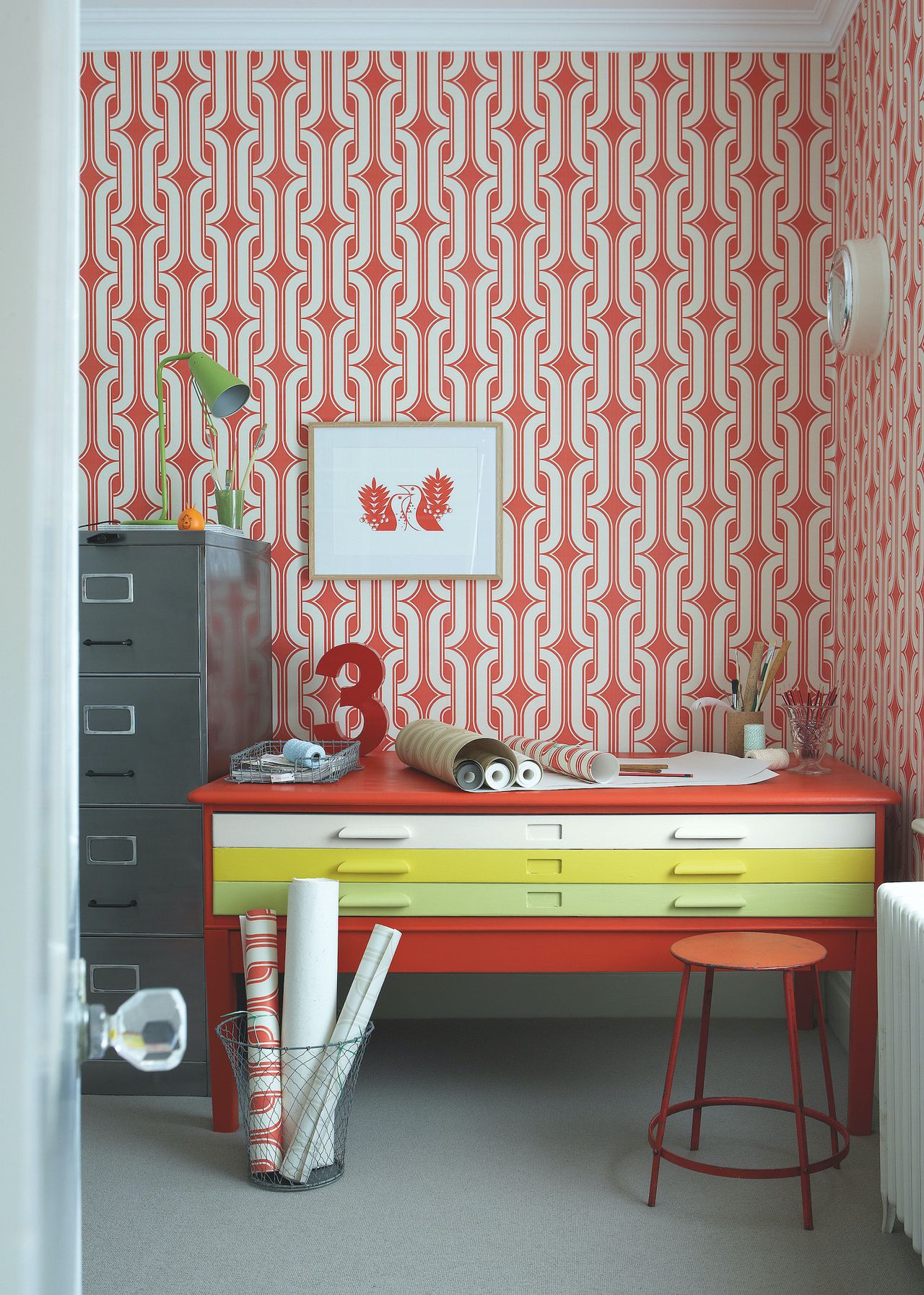 brightly coloured home office with vintage painted desk in multiple colours and red patterned wallpaper 