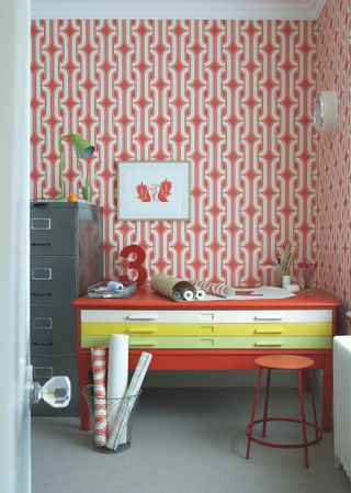 brightly coloured home office with vintage painted desk in multiple colours and red patterned wallpaper