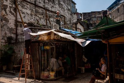 A man (top) uses rope to secure the roof of a shop before the expected arrival of Super Typhoon Mangkhut in Macau on September 15, 2018. 