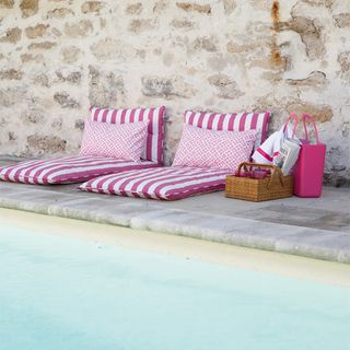 Pink and white candy stripe lounge cushions and rattan caddy on poolside patio
