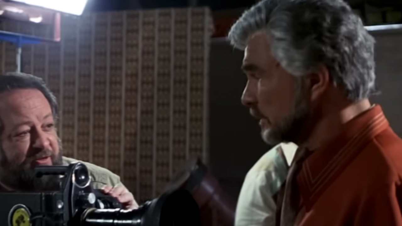 Ricky Jay holding a camera and talking to Burt Reynolds in Boogie Nights