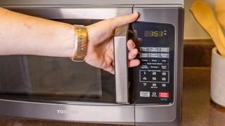 A hand pulling the door of the Toshiba EM925A5A-BS microwave open