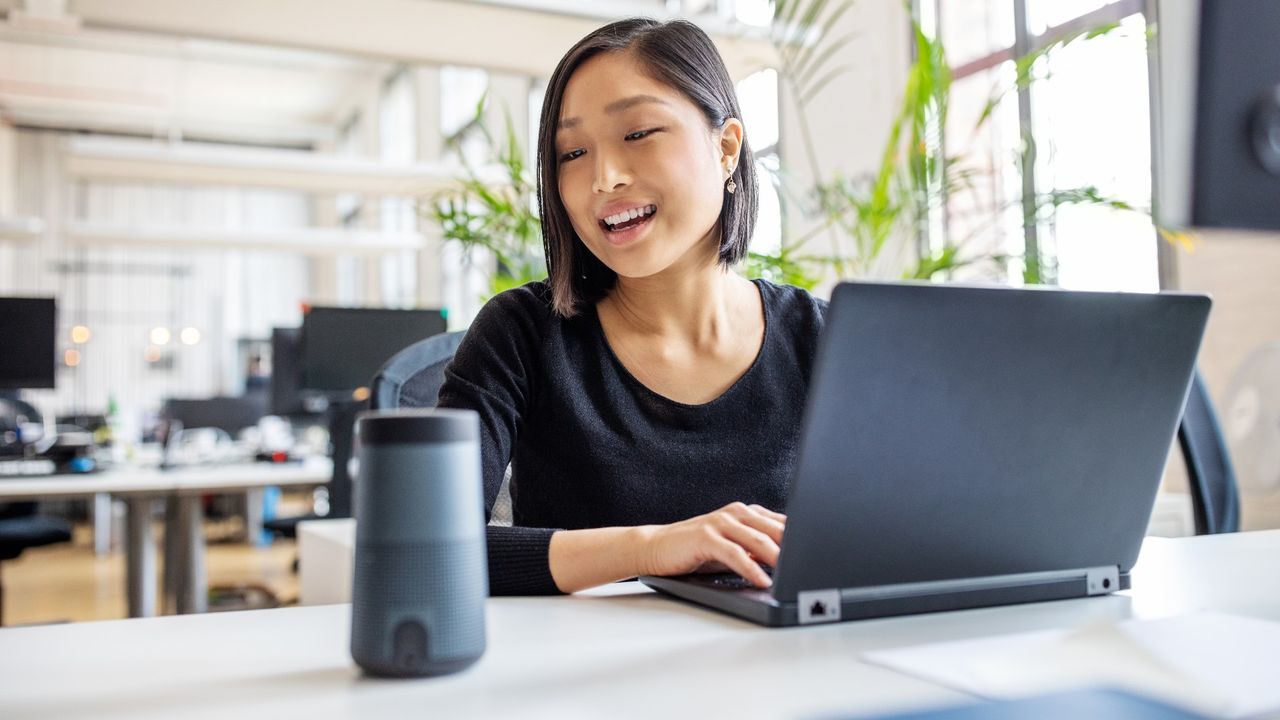 Young professional talking to virtual assistant at her desk.