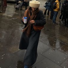 Fashion influencer @_santinaharrison wears a chic and practical look with a shearling hat and long coat that's on-trend for 2025.