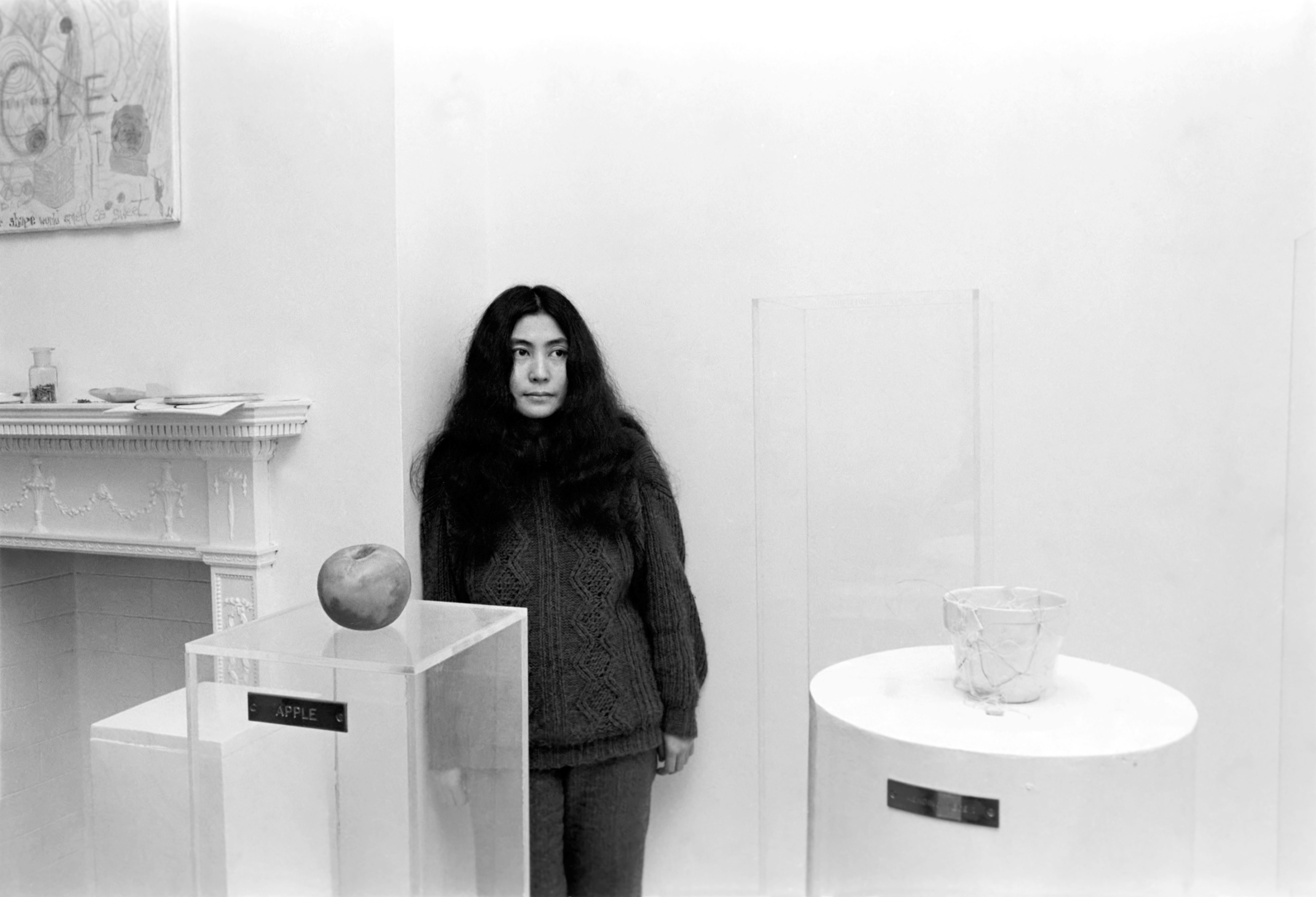 Yoko Ono stands next to art pieces in the 1960s