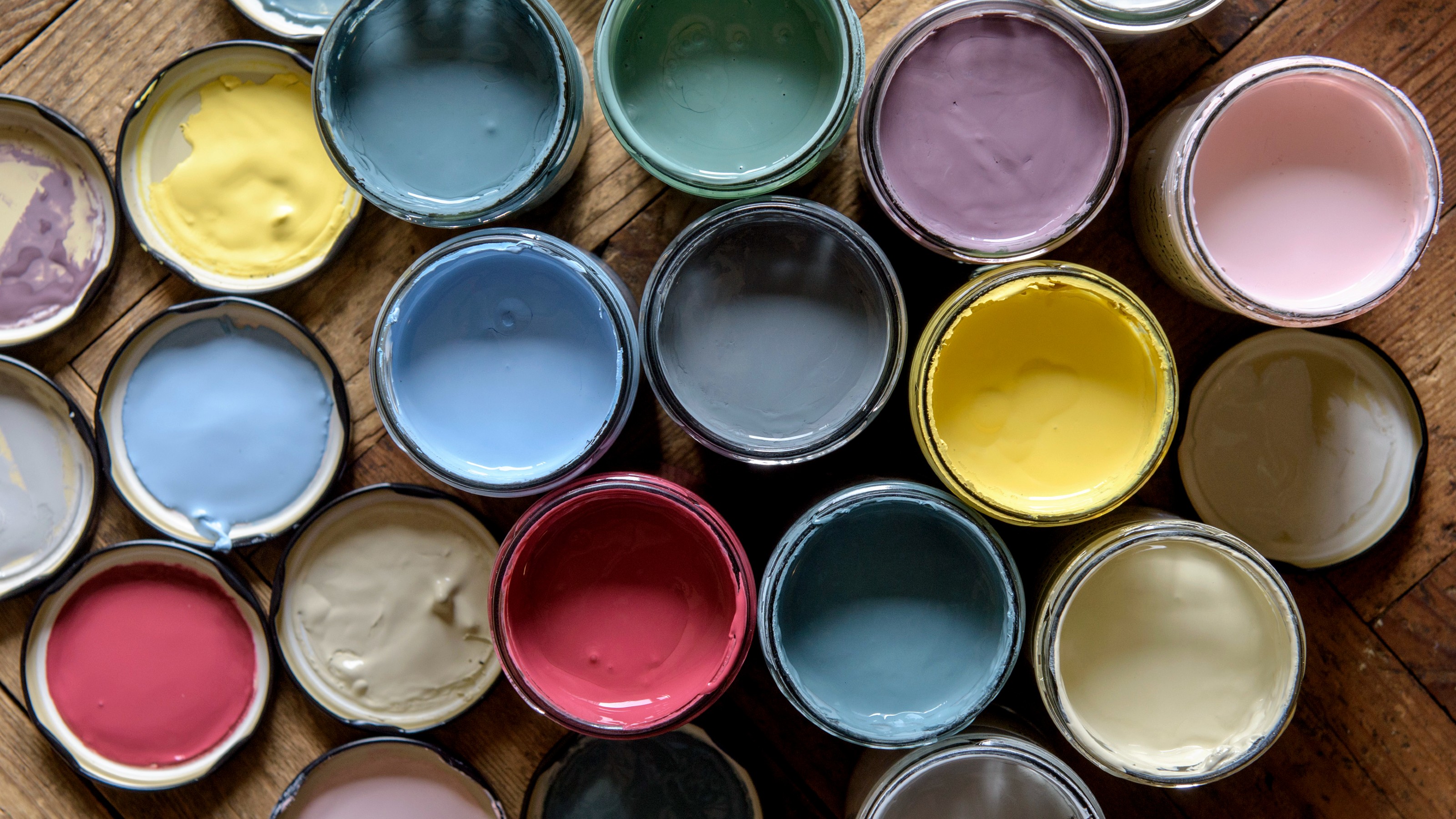 Open jars of paint in various colours on wooden flooring