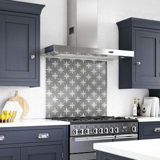Laura Ashley patterned monochrome backsplash above cooker in a dark blue kitchen with shaker cabinets