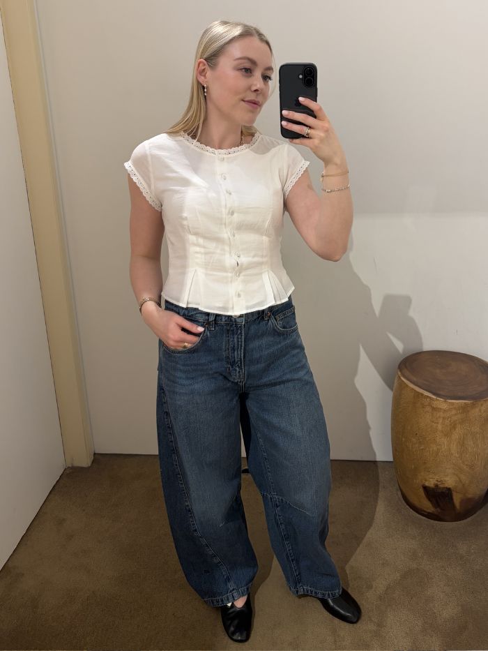 Woman wears white blouse, barrel leg jeans and ballet flats