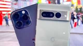 Pixel 7 Pro and iPhone 14 Pro Max in hand showing cameras at night in Times Square