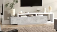 tv unit with shelves and concrete slab styled with vases and candlesticks and coffee table books, blonde herringbone floors, a rug, and a wall-mounted TV above