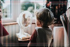 A little boy looking at a fan by the window for an article on the difference between heat stroke and heat exhaustion